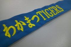 青いはちまきに鮮やかな黄色の糸でスポーツチーム名を刺繡した制作事例。