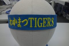 青いはちまきに鮮やかな黄色の糸でスポーツチーム名を刺繡した制作事例をマネキンの頭部に巻き付けた画像。