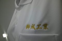 白ポロシャツの左胸に金糸で企業名を刺繡した制作事例のアップ。