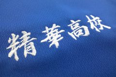 青のポロシャツの左胸に白糸で学校名を刺繡した制作事例の学校名部分のアップ。