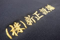 お持ち込みの黒のポロシャツの左胸にメタリック金糸で会社名をネーム加工した制作事例。書体は行書体を使用。