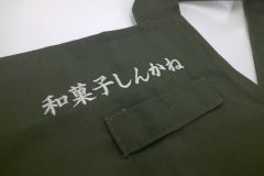 和菓子店で使用するカーキ色のエプロンの胸当て部分に店名を刺繡した制作事例。