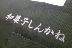 和菓子店で使用するカーキ色のエプロンの胸当て部分に店名を刺繡した制作事例の別角度。