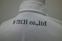 お持ち込み白いポロシャツの背面衿下に黒糸で会社名をネーム刺繡した制作事例のアップ。