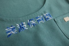緑色のエプロンに青と白のグラデーション糸で保育園名を刺繡した制作事例。