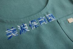 緑色のエプロンに青と白のグラデーション糸で保育園名を刺繡した制作事例。