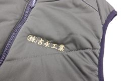 グレーのお持ち込みのダウンベストの左胸に金糸で企業名を刺繡した制作事例。