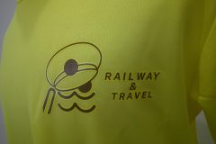 黄色のTシャツの左胸に『RAILWAY & TRAVEL』の文字と帽子をモチーフにしたシンプルな茶色のロゴが加工されたフルカラー転写の制作見本のアップ。