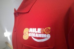赤いポロシャツの左胸に『SMILE CLEANING』のロゴ。黄色いスマイルマークと白い笑顔ラインが印象的なフルカラー転写プリントの制作実績のアップ。
