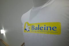 白い長袖シャツの胸元に『Baleine』のロゴ。黄色い長方形の背景に青い文字と白いクジラのイラストが描かれたフルカラー転写プリントの制作見本のアップ。