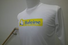 白い長袖シャツの胸元に『Baleine』のロゴ。黄色い長方形の背景に青い文字と白いクジラのイラストが描かれたフルカラー転写プリントの制作見本。
