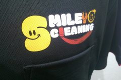 黒いポロシャツの左胸に『SMILE CLEANING』のロゴ。黄色いスマイルマークと赤い笑顔ラインが印象的なフルカラー転写プリントの制作実績のアップ。