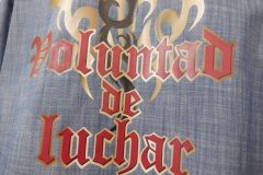 淡いブルーデニムシャツの背面に、金と黒のトライバル模様と赤いゴシック文字『Voluntad de luchar』が加工されたフルカラー転写プリントの制作事例のアップ。