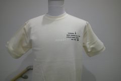アイボリーの裾ドローコード付きTシャツの左胸にネイビーのシートで、社名や取扱い業務、創業年などをデザインしたマークをプリントしたラバープリントの制作実績。全体を表示。