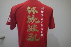 赤いドライTシャツの背中全面にメタリックゴールドのシートで、道場理念が躍動感ある筆文字で縦に大きくデザインされており、その横に白いシートで道場支部名がプリントされたラバープリントの制作実績。ウェアー全体を表示。