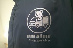 ネイビーのブルゾンの左胸に、メタリックシルバーのシートで運送会社のシンボルマークと社名ロゴをプリントしたラバープリント部分のアップ。
