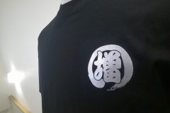 黒いTシャツの左胸にグリッターシルバーのシートで運送会社のシンボルマークをプリントしたラバープリント部分のアップ。