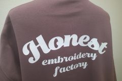 モーブのトレーナーの背中全面に白いシートで大きく「Honest」のロゴを配置したラバープリントのアップ。