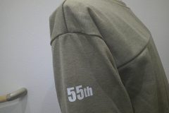 杢グレーのトレーナーの右袖上部に白いシートで55周年マークのワンポイントをプリントしたラバープリントの制作実績。