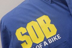 青いボタンダウンのシャツの右胸に黄色と白いシートでロゴをプリントしたラバープリント部分のアップ。