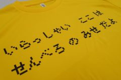 鮮やかな黄色のTシャツに黒いシートで立ち飲み屋の雰囲気を、レトロゲーム風のピクセル文字で表現したデザインをプリントしたラバープリント部分のアップ。