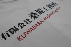 白いカノコポロシャツの背中中央に黒と赤いシートで会社名をプリントしたラバープリント部分のアップ。