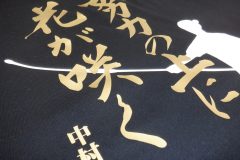 黒いドライTシャツの背中全面に白いシートで人物のシルエット、メタリックゴールドのシートで教育理念と学校名、部活名をプリントしたラバープリント部分のアップ。シートを重ねてプリント圧着することで奥行きを表現している。