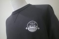 黒のトレーナー左胸に円形をベースとしたロゴのオリジナル刺繍を加工した制作事例。糸色はホワイト。