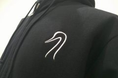 黒のフルジップパーカーの左胸に銀糸で白鳥のシルエットロゴを刺繍した、刺繍屋HONESTの制作事例。