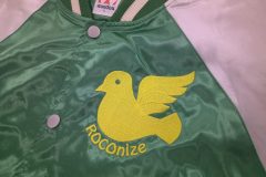 スタジャンの左胸に黄色の糸で鳥のロゴと英字をタタミ縫いを主軸に刺繍した加工事例。