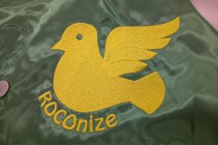 スタジャンの左胸に黄色の糸で鳥のロゴと英字をタタミ縫いを主軸に刺繍した加工事例のアップ。