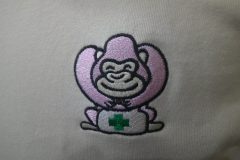 ベージュカラーのトレーナーの左胸に薬箱を持ったかわいいゴリラのキャラクターをオリジナル刺繍として加工した制作事例のアップ。