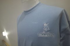 淡いブルーのTシャツの左胸にリフォーム会社のロゴを白糸で刺繍をした制作事例。