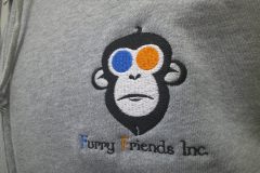 グレーのフルジップパーカー左胸に白・橙・青・黒で企業ロゴをオリジナル刺繍として加工した制作実績のアップ。