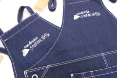 デニムエプロンの胸中央にサンドイッチ店の店名とサンドイッチのワンポイントデザインを白単色で刺繍した制作実績。