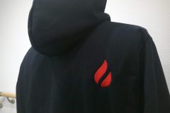 パーカー背面右肩へ赤糸で炎を示すワンポイントロゴを刺繍した制作事例。