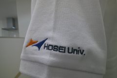 白の鹿の子ポロシャツ左袖に大学のロゴを三色で刺繍した制作事例のアップ。
