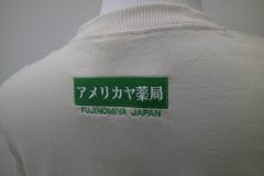お持ち込みのTシャツの背面衿下に緑糸でボックスロゴを刺繍。その下には地域名を文字刺繍した制作事例のアップ。