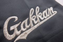 ドライゲームシャツの左袖口に学校のロゴを銀糸で刺繍した制作事例のアップ。サテン縫いによるふっくら感が特徴。