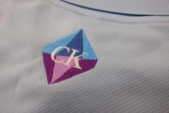 ポロシャツの背中衿下に学校の校章ロゴを、水色・青・薄紫・紫・白の5色で刺繍加工した制作事例のアップ。