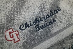グレーと白のグラデーションタオルに赤糸・白糸・紺糸で野球チームのロゴを刺繍した制作事例。