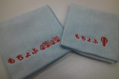 薄い水色のハンドタオル2枚にそれぞれ企業ロゴとトラックのモチーフと企業ロゴと気球のモチーフを赤糸で刺繍した制作実績。