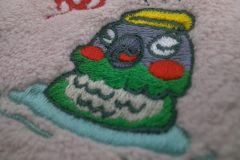 ピンク色のタオルに鳥が温泉に浸かっている様子をモチーフにした刺繍の制作事例の加工部品のアップ。