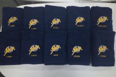 お持ち込みの紺のタオルに部活動のチームロゴを山吹色と白糸で刺繍加工をした制作実績。ロゴの下には個人名刺繍入り。