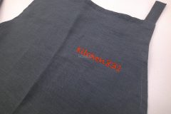 炭黒のエプロンに赤糸でオリジナルロゴ文字が刺繡された制作事例。