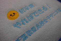 パステルカラーのオレンジ色と水色のハンドタオルに記念品として応援メッセージを刺繍した制作事例のアップ。