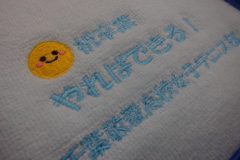 パステルカラーのオレンジ色と水色のハンドタオルに記念品として応援メッセージを刺繍した制作事例のアップ。