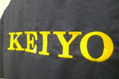 濃いネイビーのシャツの背面に企業ロゴが大きく発色鮮やかな黄色糸で刺繍された制作事例のアップ。