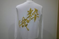 白の長袖Ｔシャツの背面に金糸で大きく文字刺繍加工された制作事例。