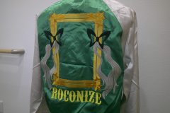 サテン地ジャケットの背面に黄色のリボン風フレームをモチーフとロゴのオリジナル刺繍の制作事例。